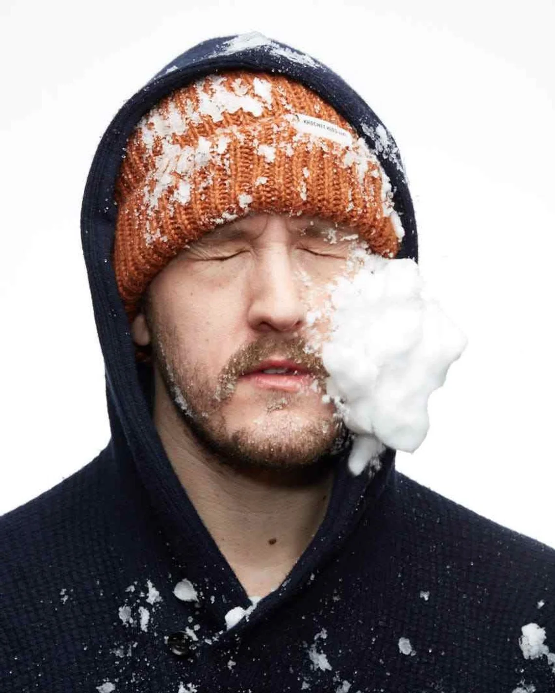 Zack DeZon, snow on his face, wearing an orange knit cap and a hood